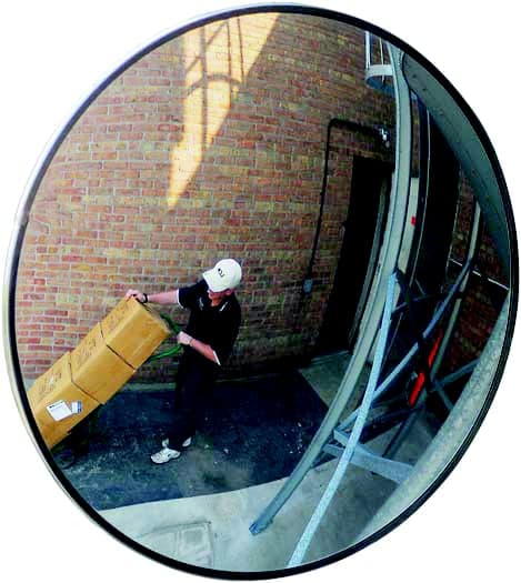 Outdoor convex mirror at a loading dock reflecting a worker moving boxes on a hand truck
