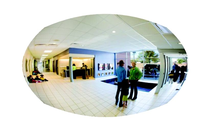 Convex mirror view of a school entrance lobby with students and parents near the front office