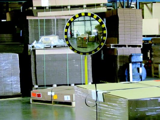 Convex mirror with a yellow and black safety border mounted on a post at a blind corner